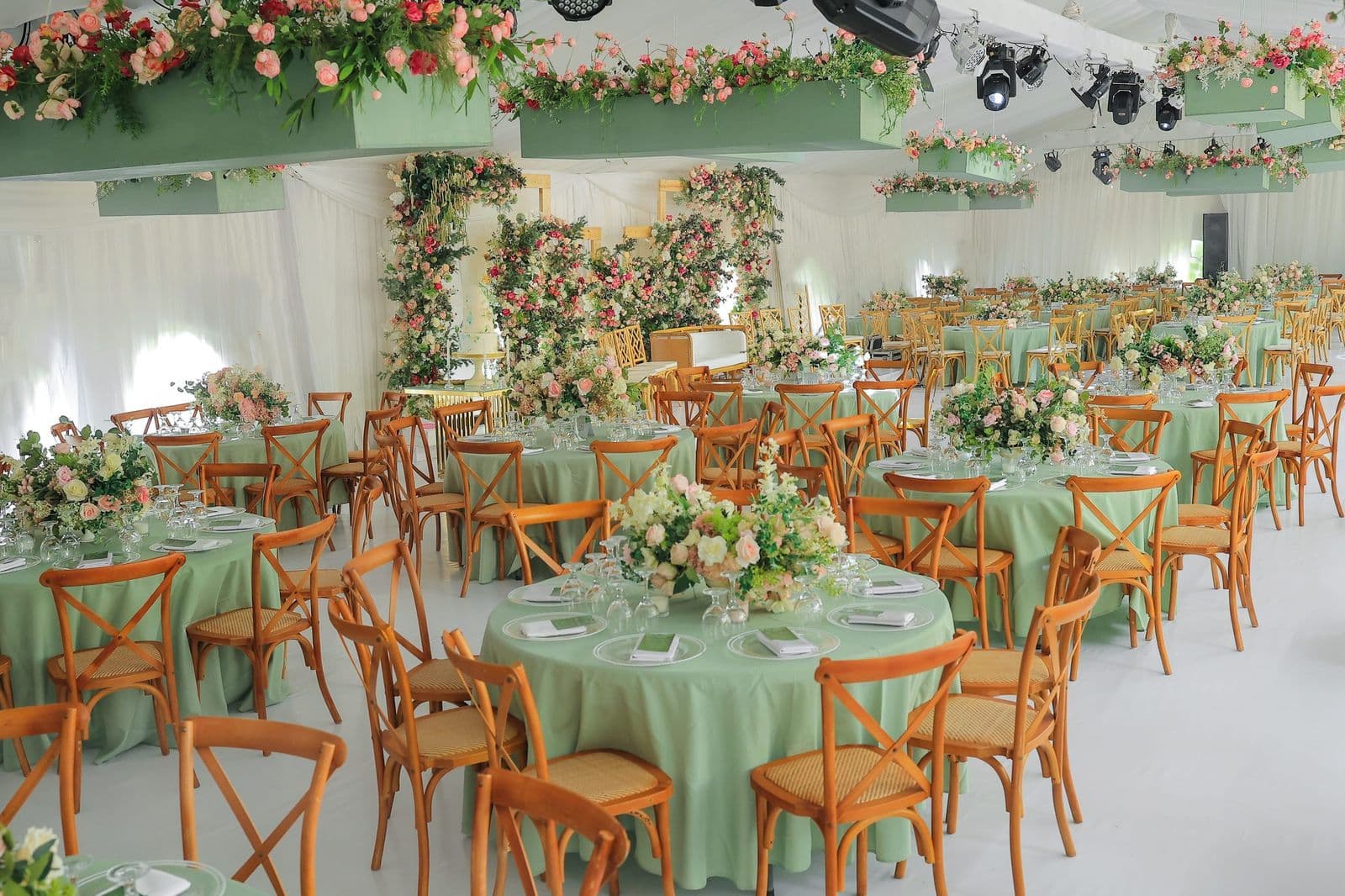 Elegant Kuhingira reception with sage green linens, pink floral chandeliers, and cross-back chairs
